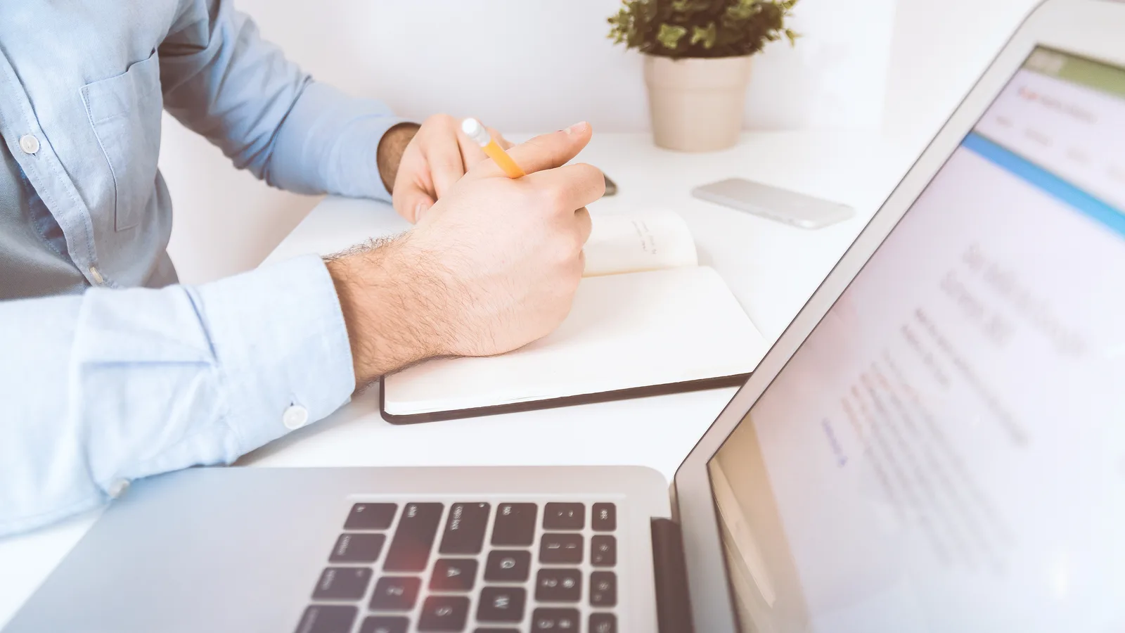 A business owner taking notes beside a laptop at an office desk, planning which AI tools to adopt