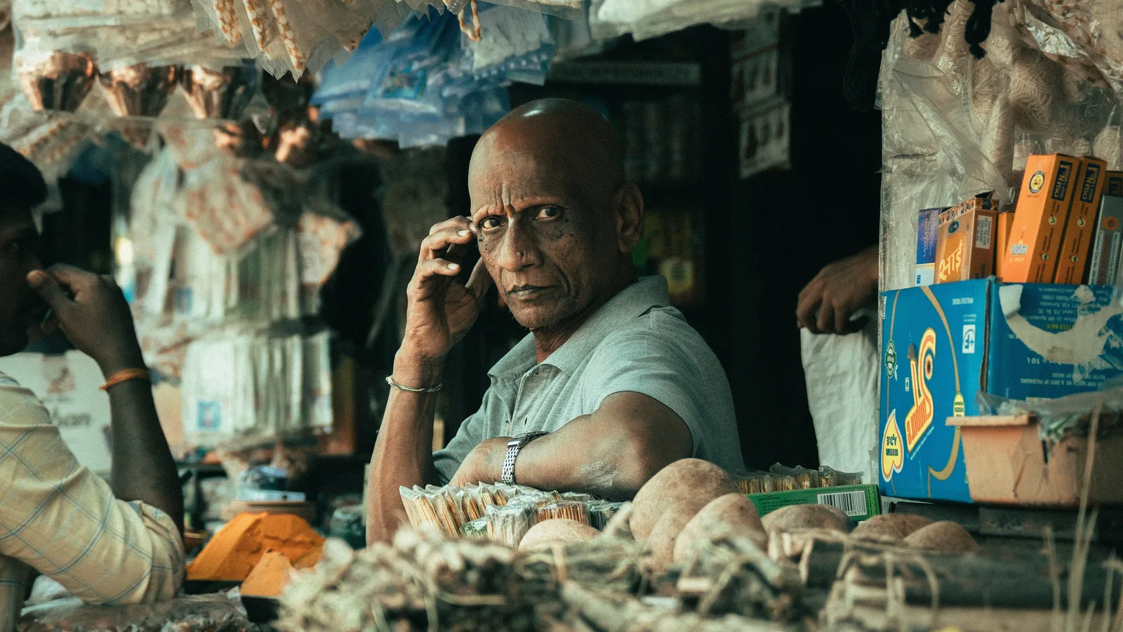 Shopkeeper seated behind the counter of a crowded general store in an Indian market