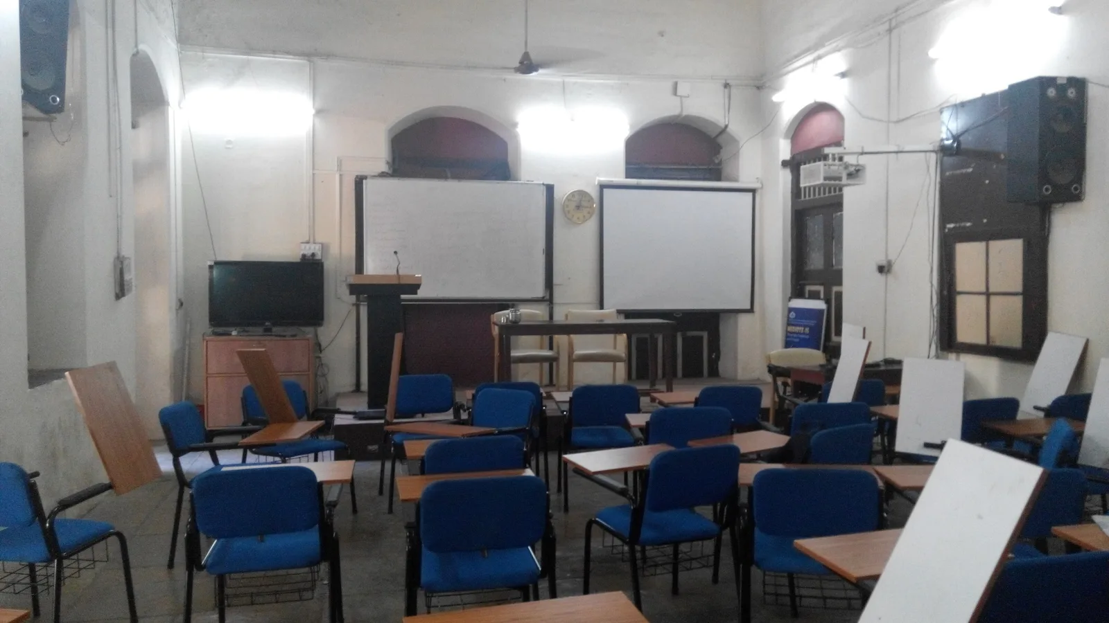 Empty lecture room with writing-pad chairs, a whiteboard and a projector screen in an Indian college