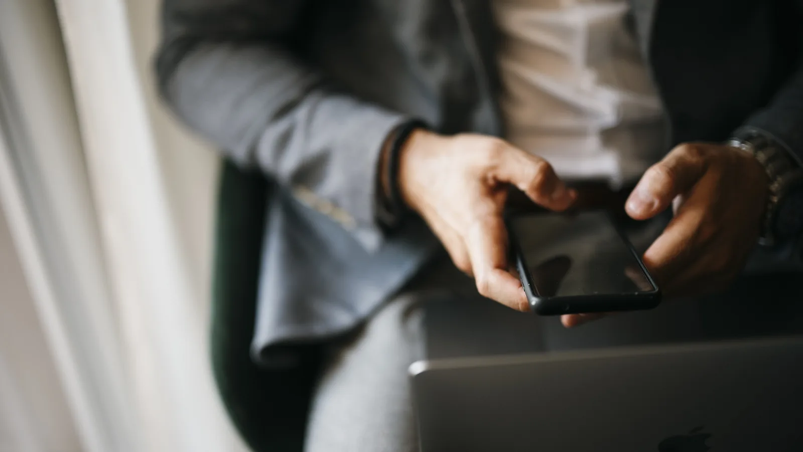 Close-up of a person typing on a smartphone while sitting with a laptop
