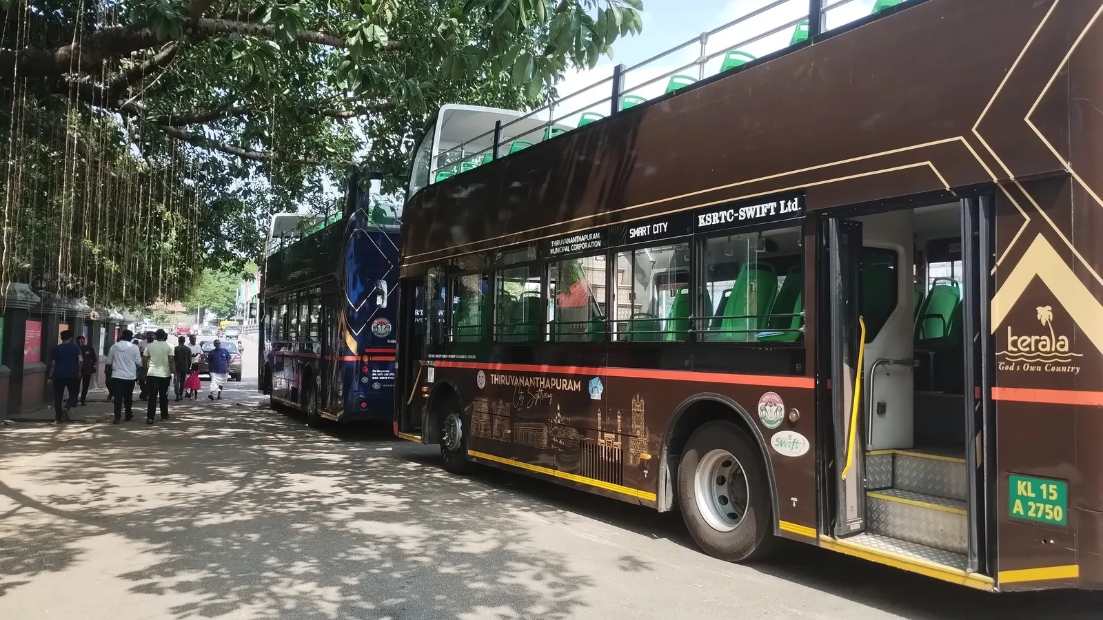 Open-top double-decker city sightseeing buses parked on a tree-lined street in Thiruvananthapuram