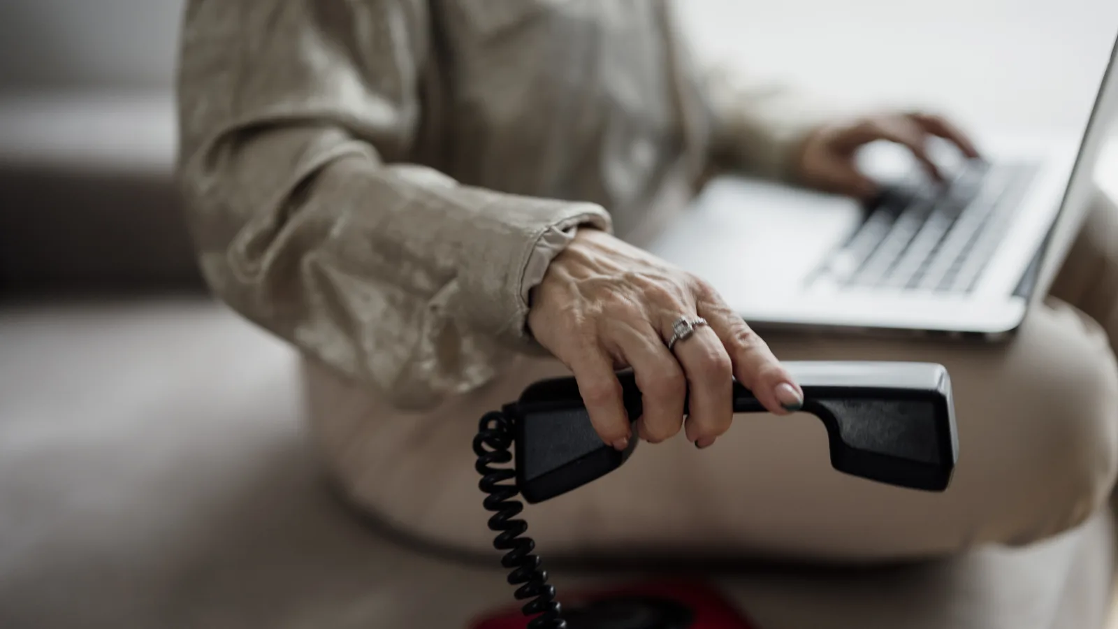 Hands typing on a laptop while holding a desk phone receiver, the everyday setup for running a small business website