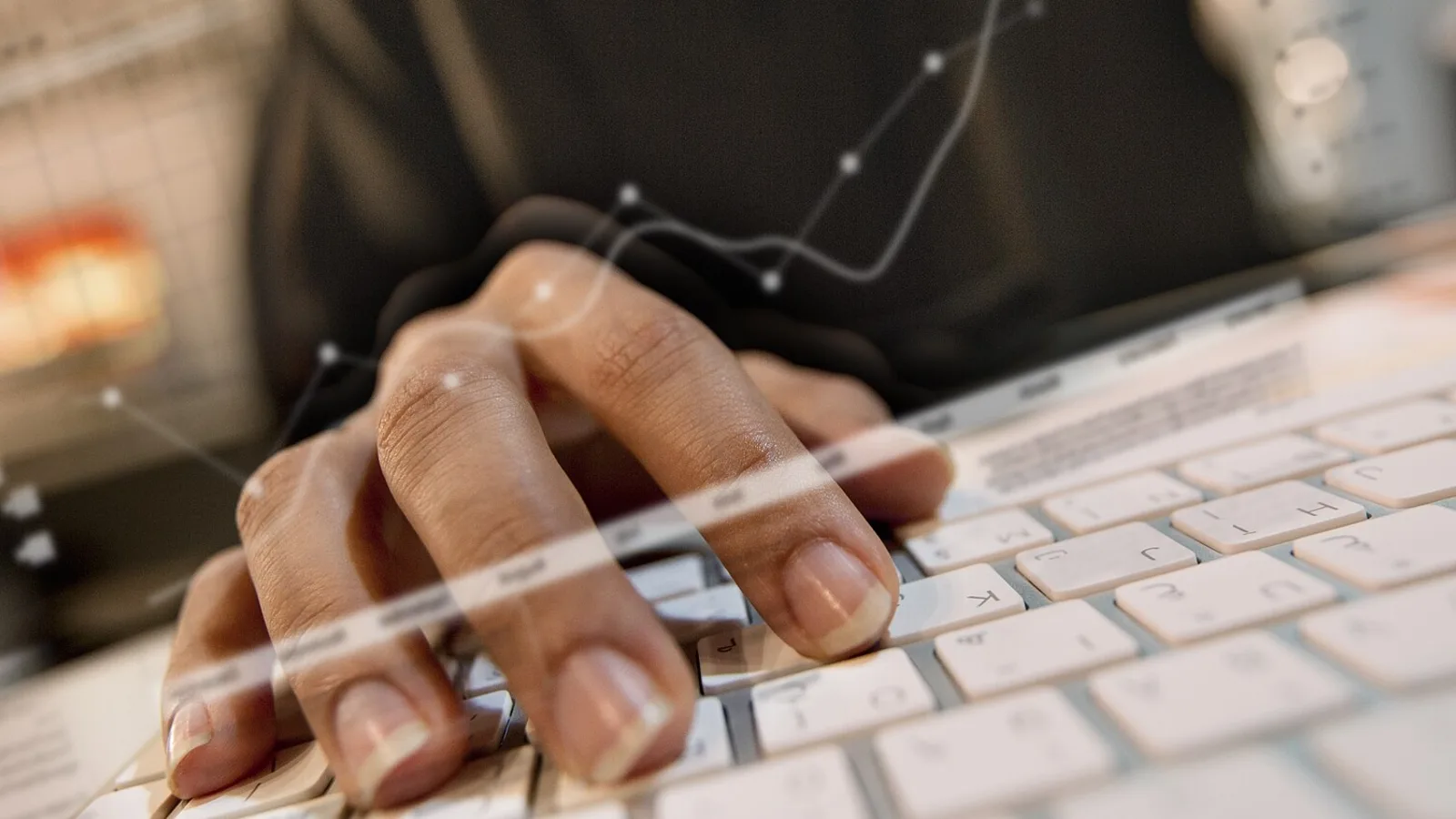 Hand typing on a keyboard with a translucent line chart overlay, suggesting business dashboards