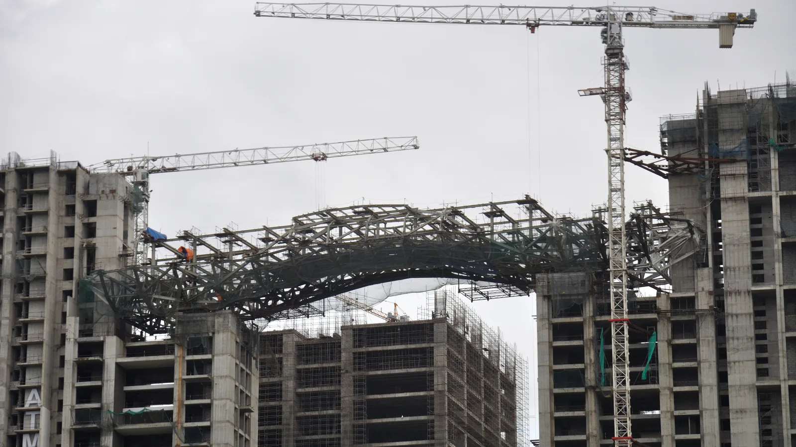 High-rise residential towers under construction in Kolkata with tower cranes and a steel roof structure being erected