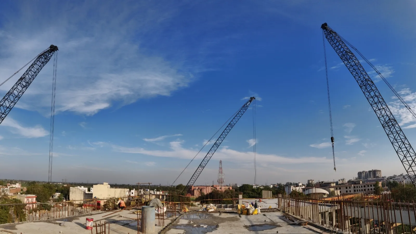Crawler cranes over a concrete roof slab at an Indian building site, with workers and materials on the deck