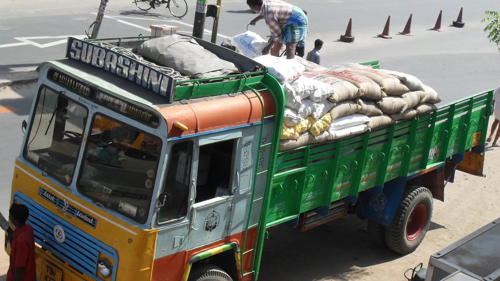 A goods lorry loaded with sacks being secured by a worker on a street in Tamil Nadu