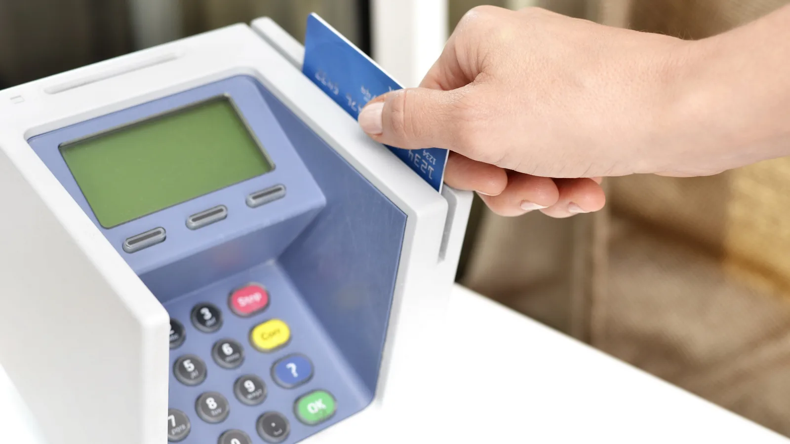 A hand inserting a blue payment card into a white card payment terminal on a counter