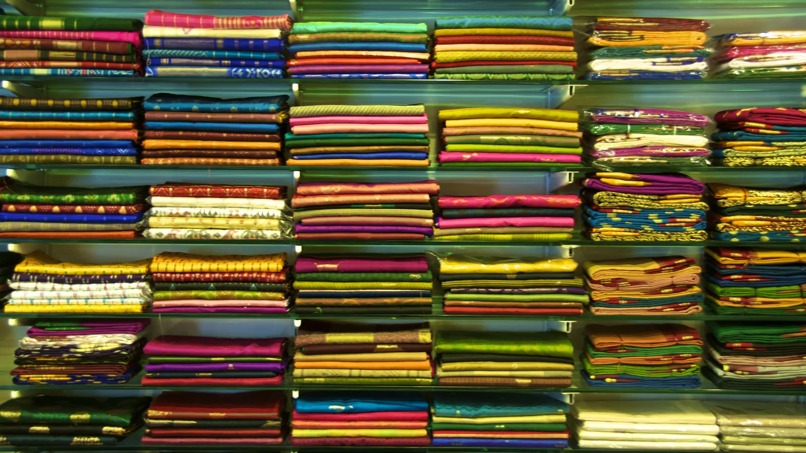 Shelves stacked with folded sarees in many colours at an Indian clothing shop