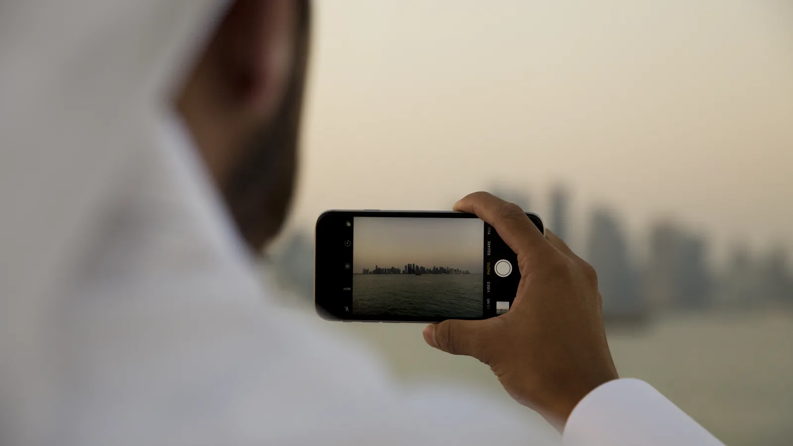 A person photographing a city skyline on a smartphone camera, the everyday tool of social media content creators