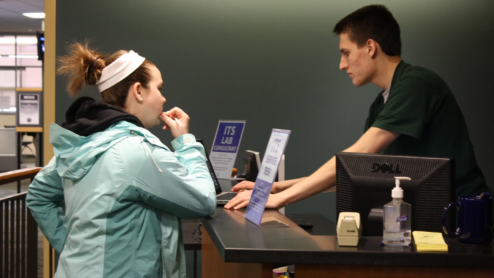 A staff member at an IT service desk helping a user at the counter