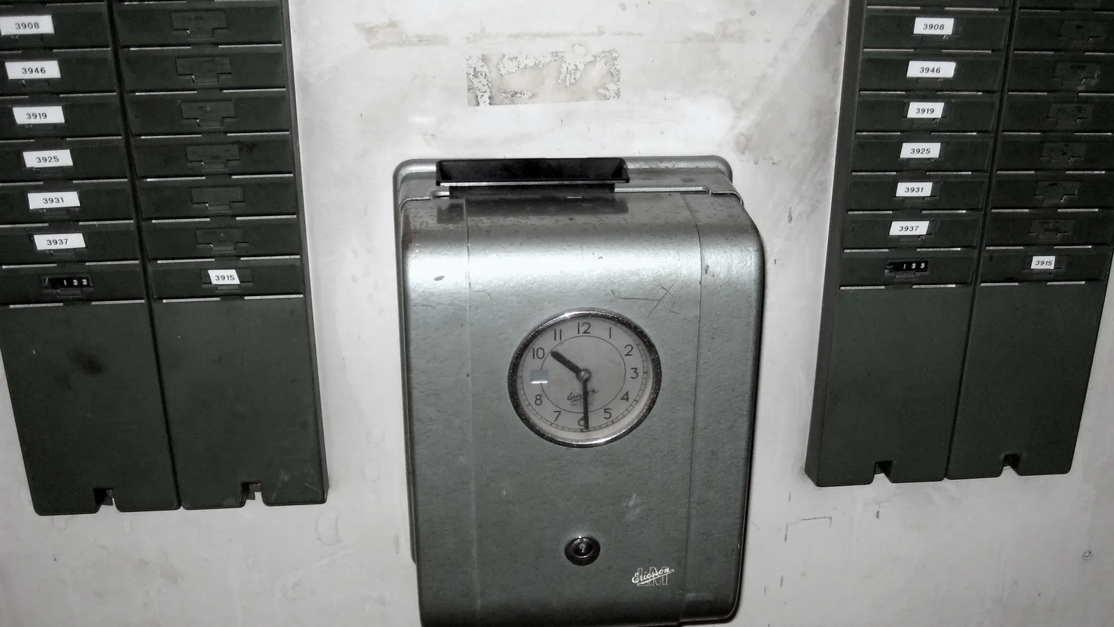 Mechanical time clock mounted between numbered punch card racks