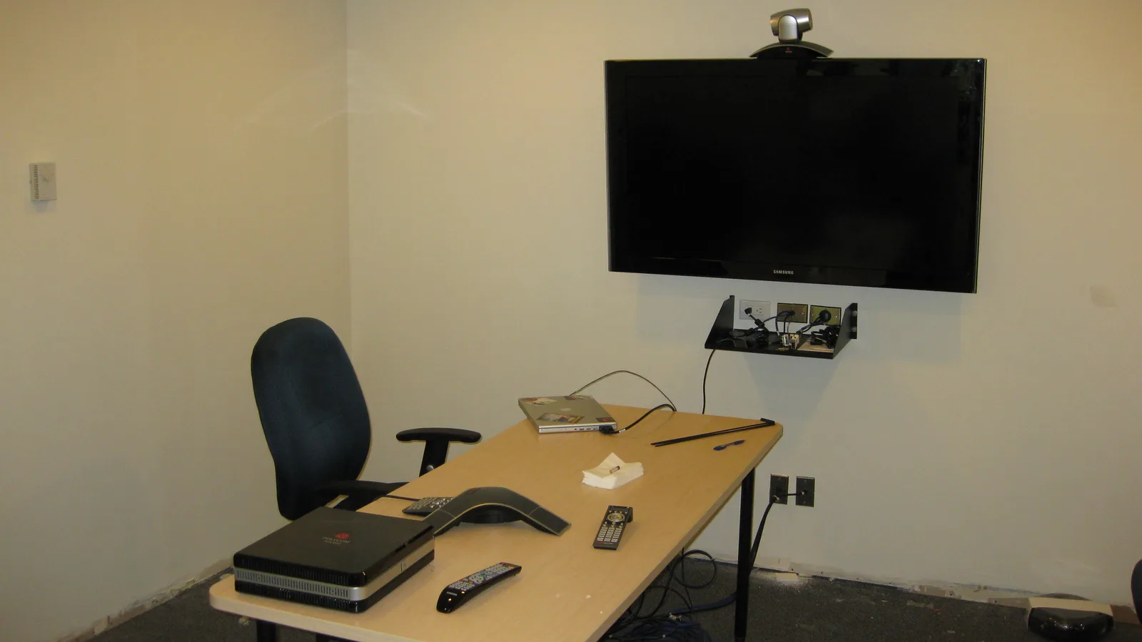 Small meeting room set up for video conferencing with a wall screen, camera and conference speakerphone