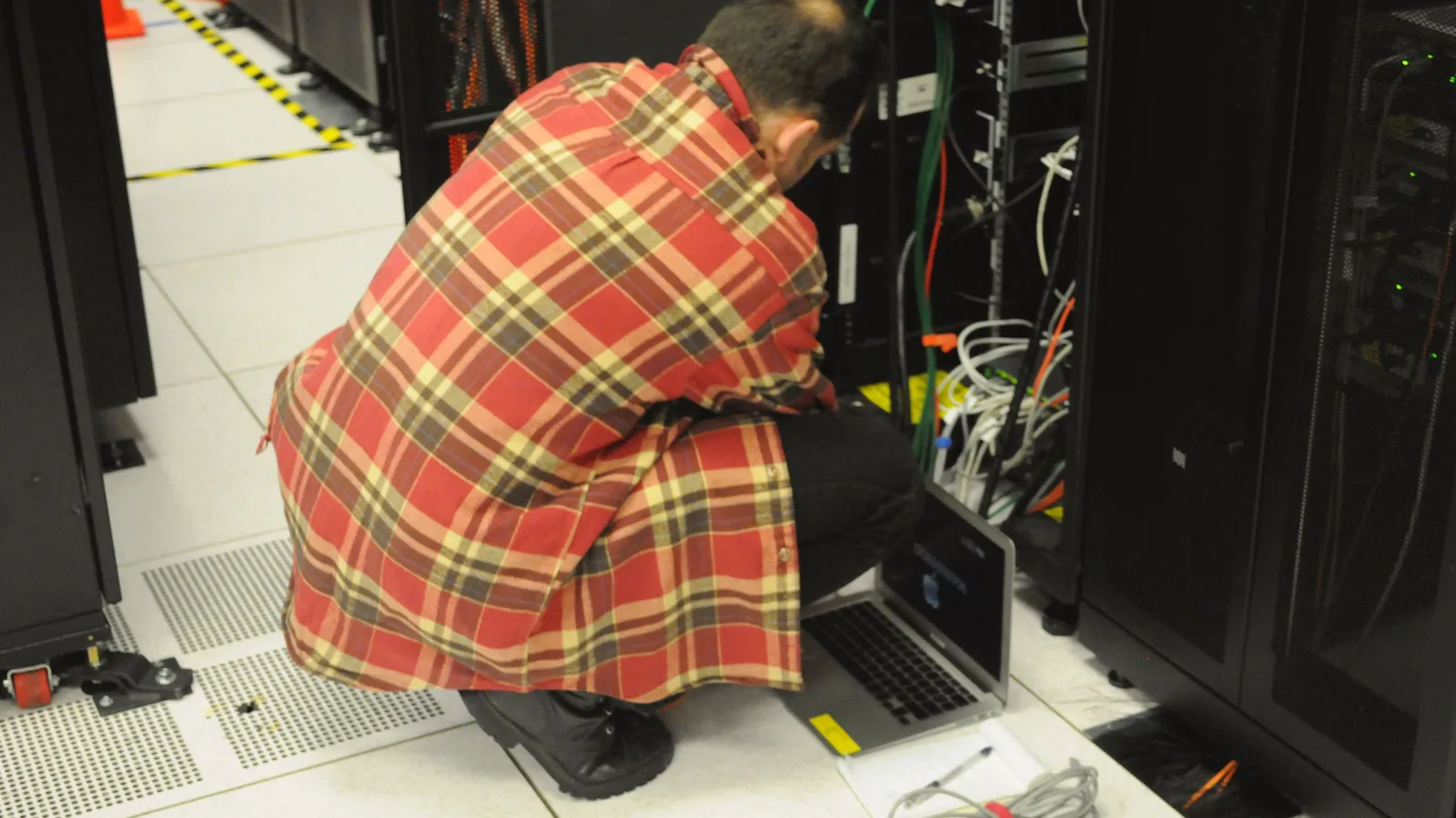 Technician with a laptop working on cabling inside a server rack in a data centre